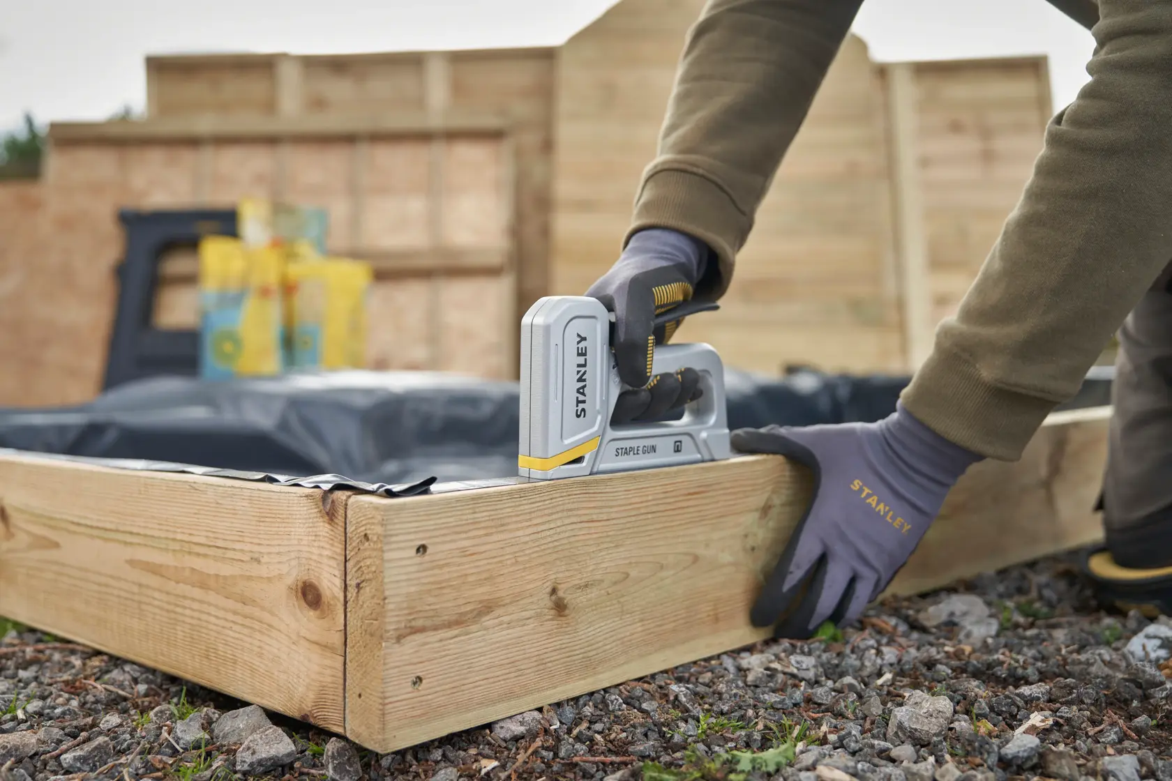 STANLEY STHT70150-0 staple gun in use, fastening plastic to wooden frame outdoors.