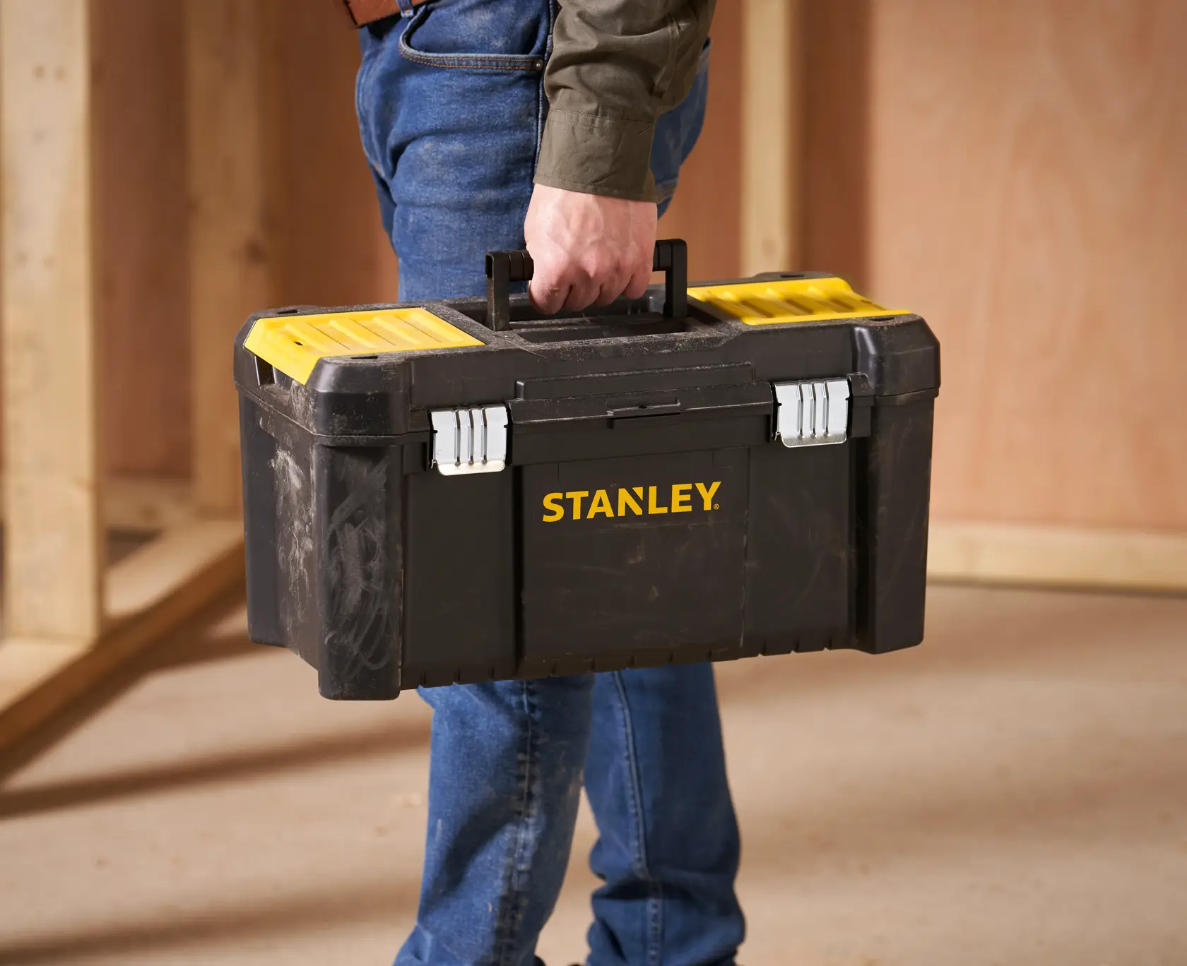 Stanley STST1-75521 black and yellow toolbox held by person, shown in workshop setting.