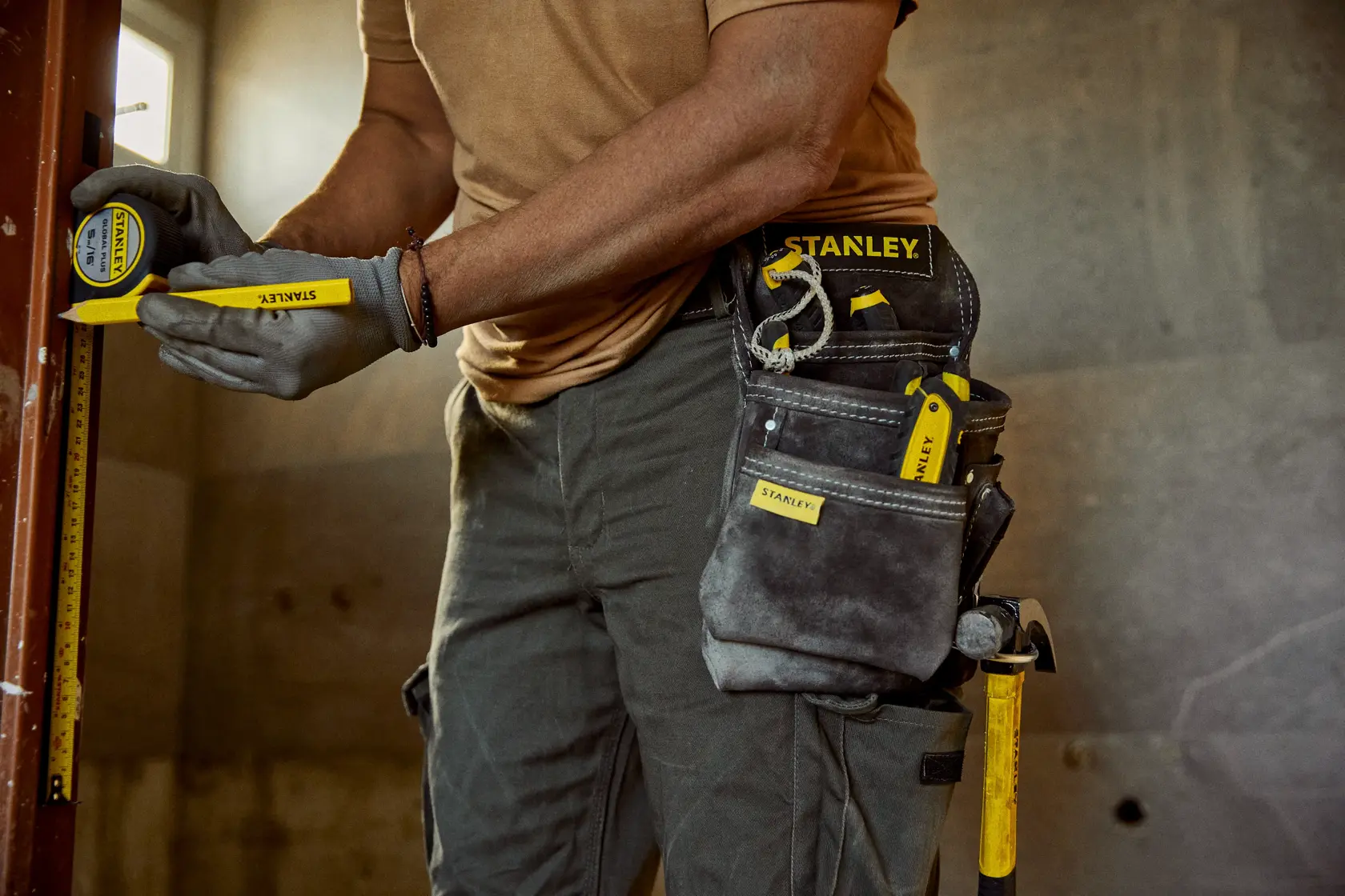 STANLEY STST1-80114 tool belt photography, showing carpenter using tape measure and marker with tool pouch and gloves.