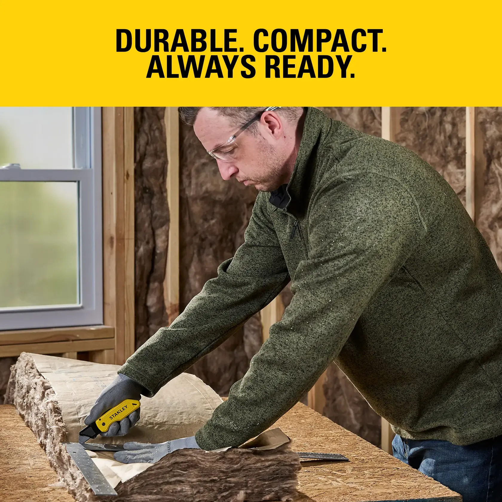 Person using a Stanley utility knife to cut insulation on a workbench in a construction area.