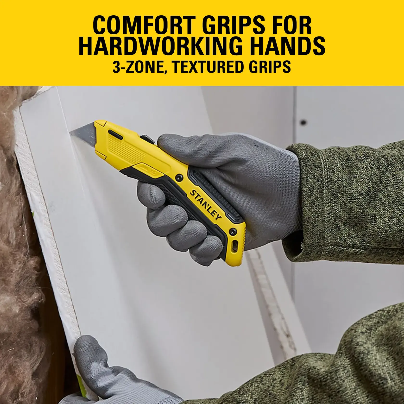 Stanley utility knife with comfort grips, held by a gloved hand cutting drywall.