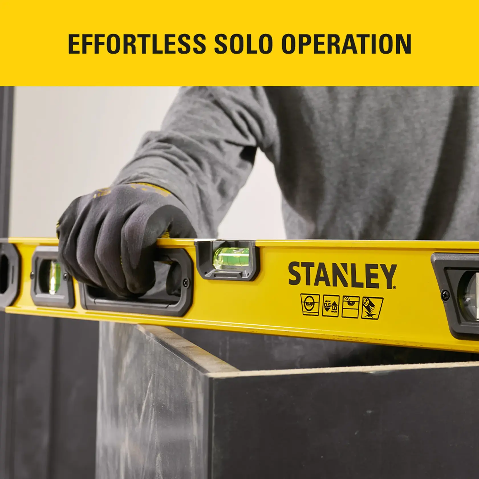 Photo of STANLEY STHT41024-0 spirit level in use by gloved hand, yellow body with brand logo, close-up view.