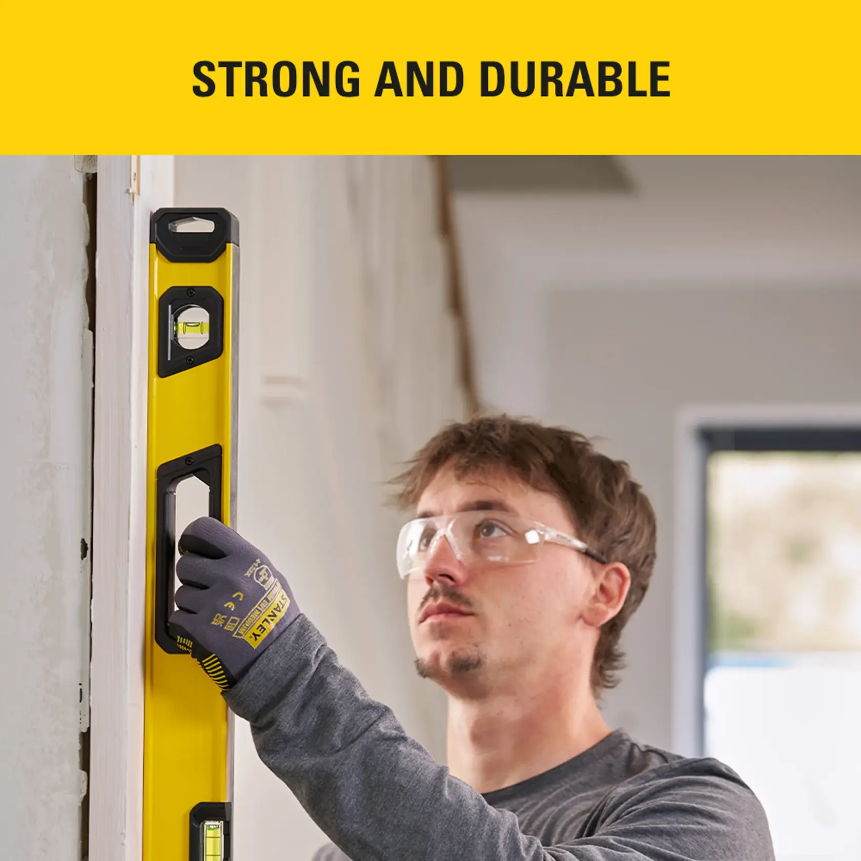 Photo of a man using a STANLEY STHT41036-0 level tool on a wall indoors, wearing safety glasses.