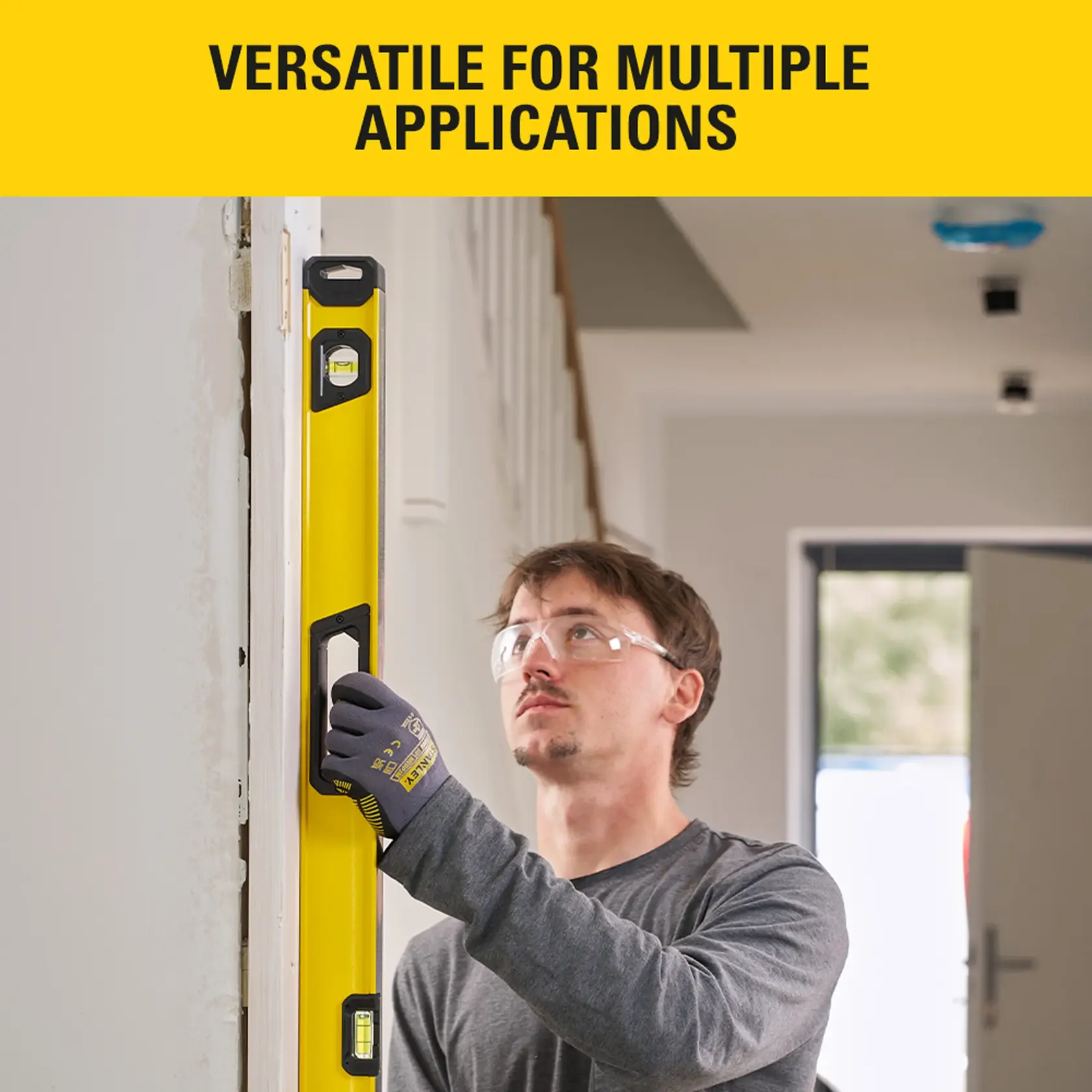 STANLEY STHT41048-0 spirit level used vertically on door frame by person wearing gloves and safety glasses.