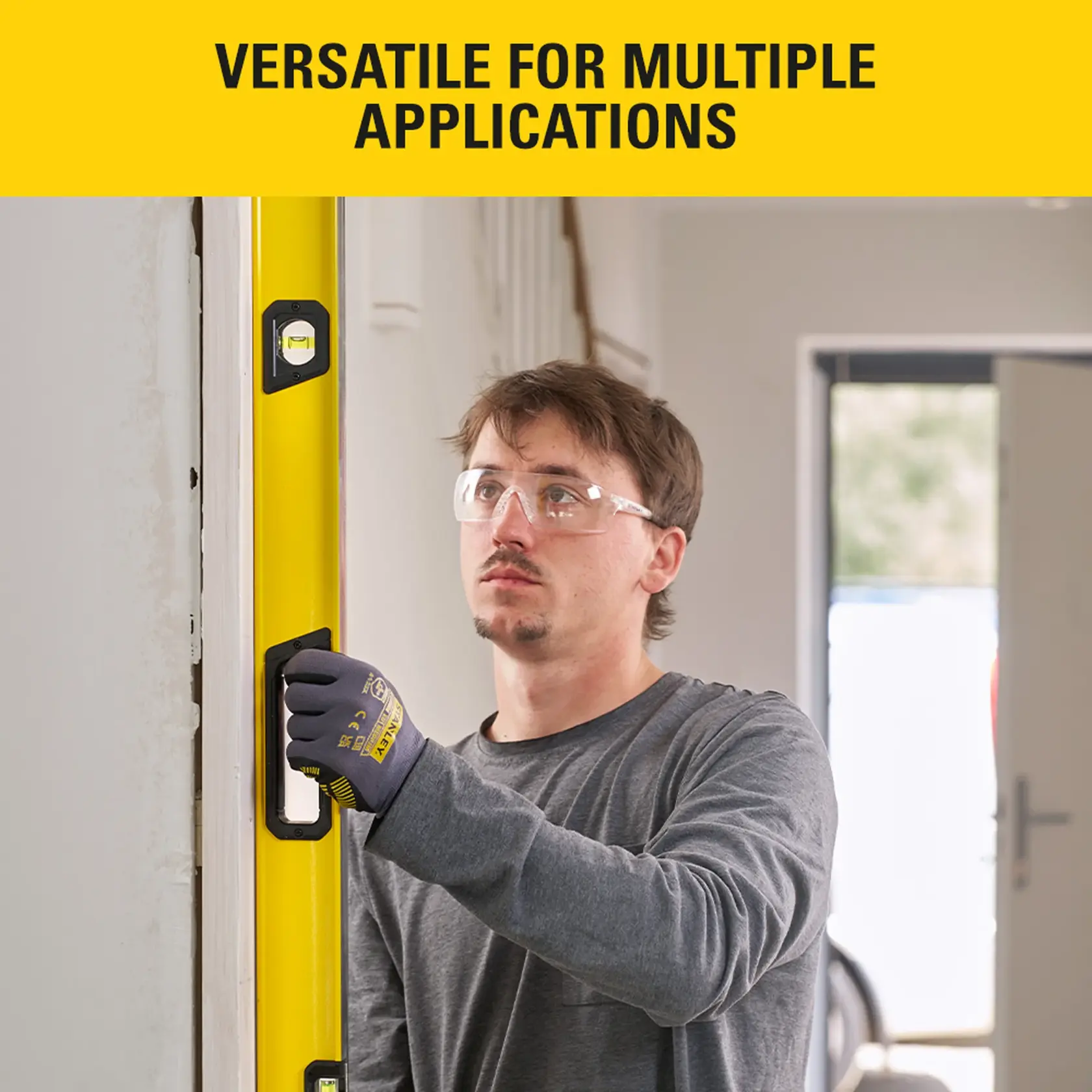 Person using STANLEY STHT41072-0 spirit level indoors with safety glasses and gloves.