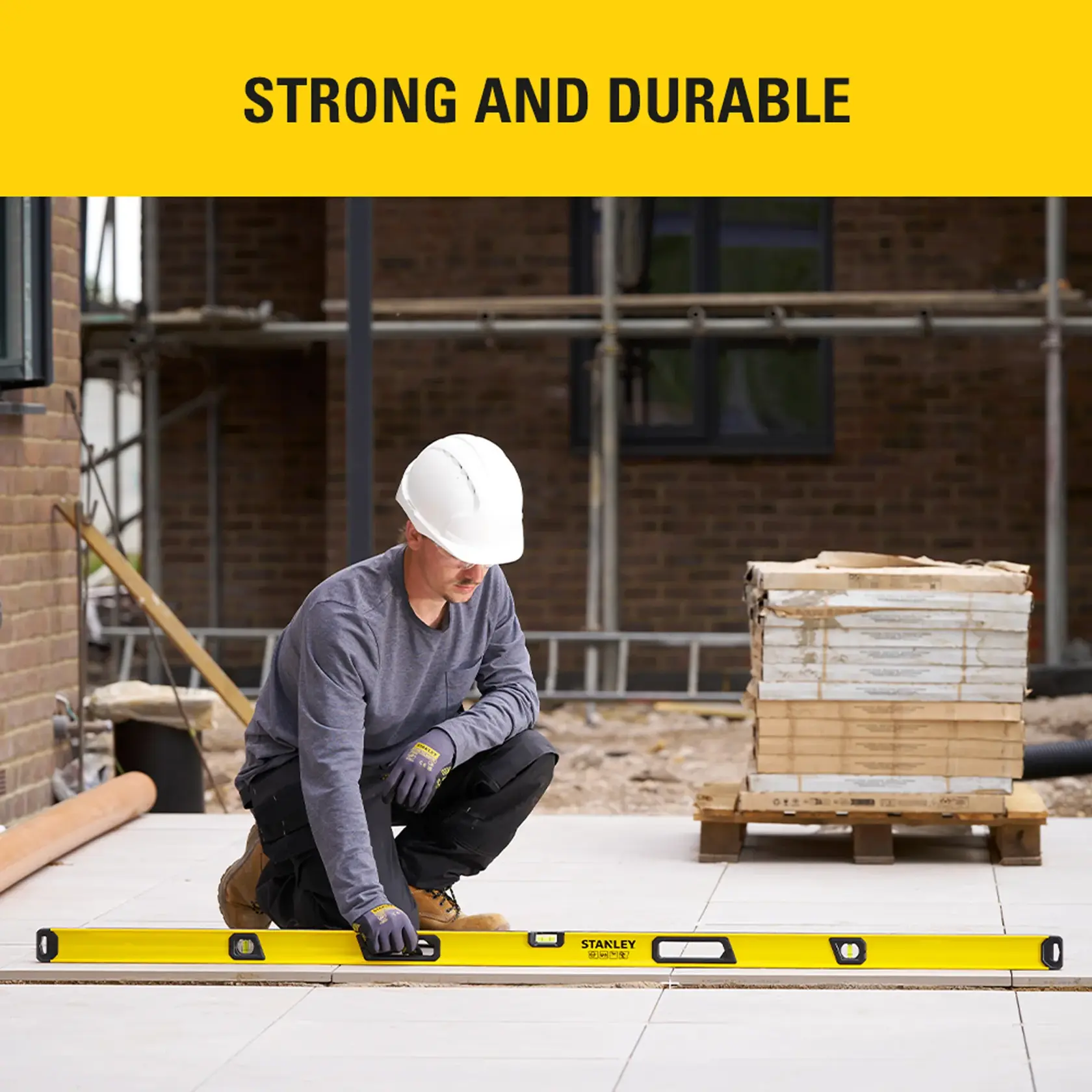Stanley STHT41072-0 spirit level used by worker at construction site, yellow body, outdoor setting.