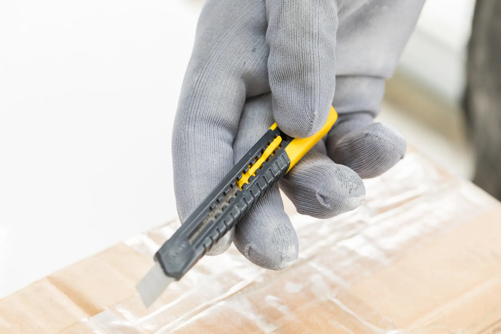 STANLEY 0-10-150 utility knife with grey gloves cutting tape on a cardboard box, close-up photography.