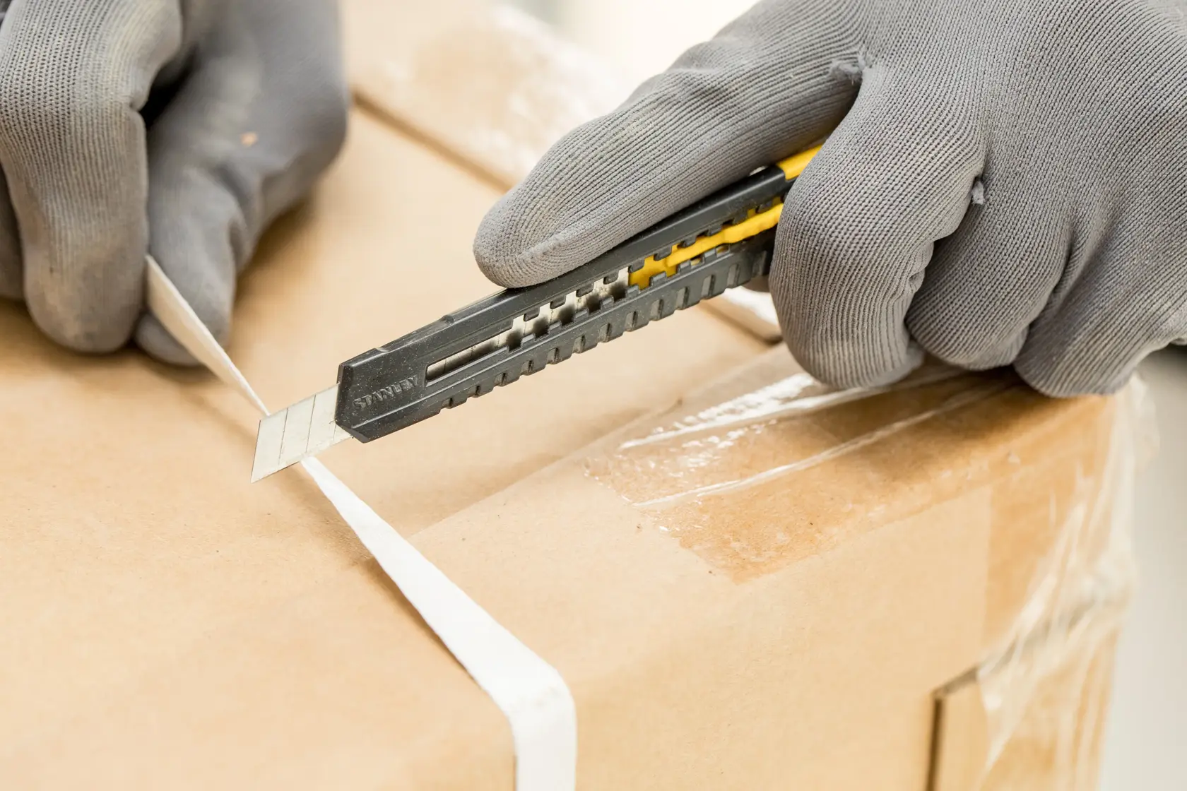 STANLEY 0-10-150 utility knife cutting white strap on cardboard box, handheld, close-up photography.