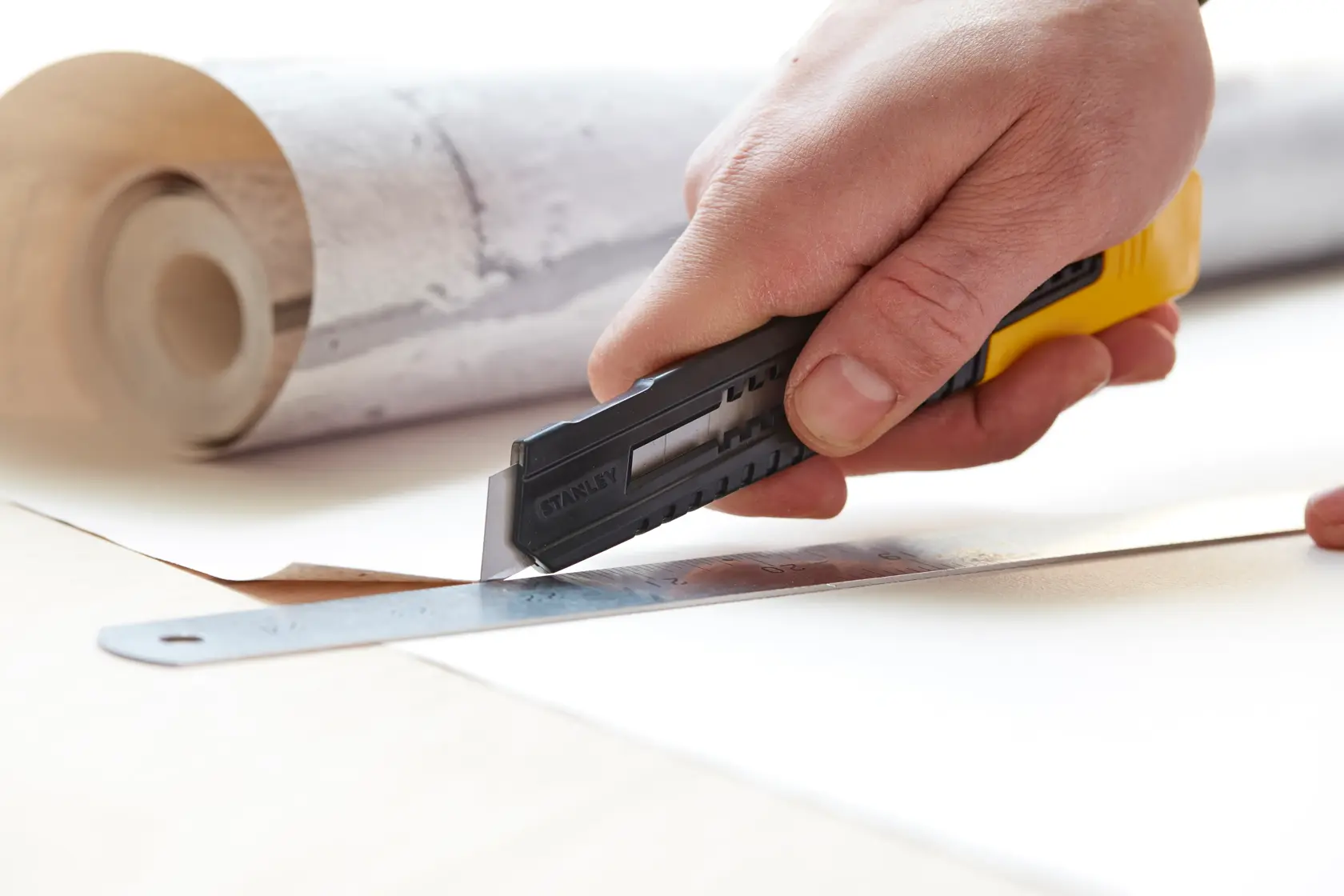 STANLEY 0-10-151 utility knife cutting wallpaper with ruler, close-up photo, hand holding tool.