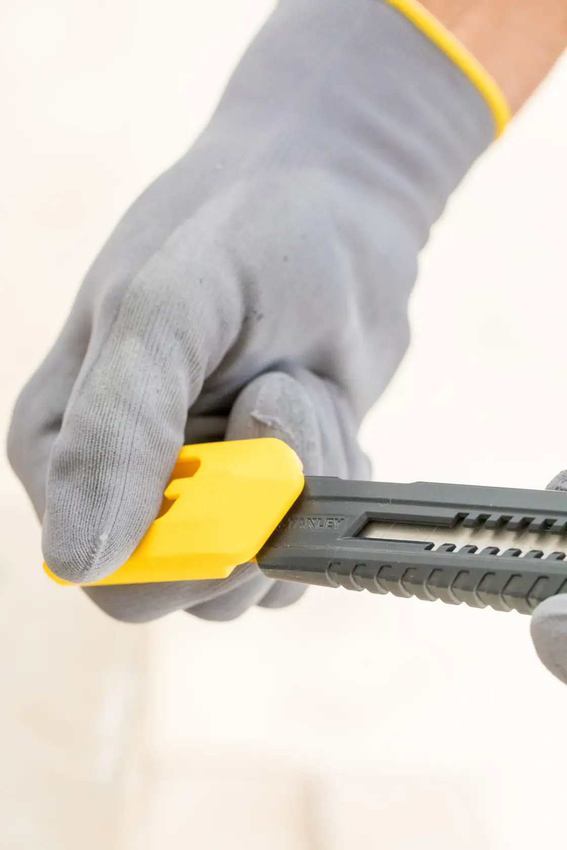 Photo of STANLEY 0-10-151 snap-off knife with black handle and gray blade, held by gloved hands, with yellow covers nearby.