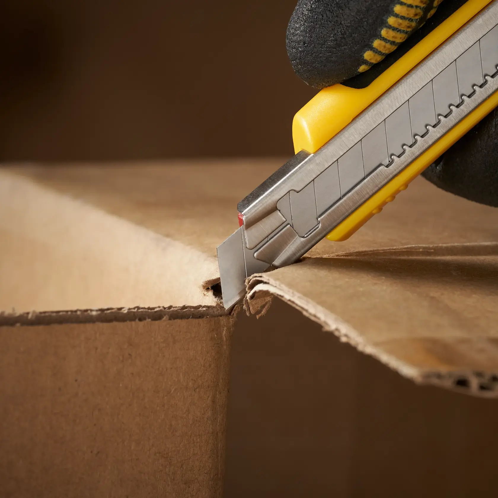 Photo of STANLEY 0-11-300 utility knife cutting cardboard box, close-up side view.