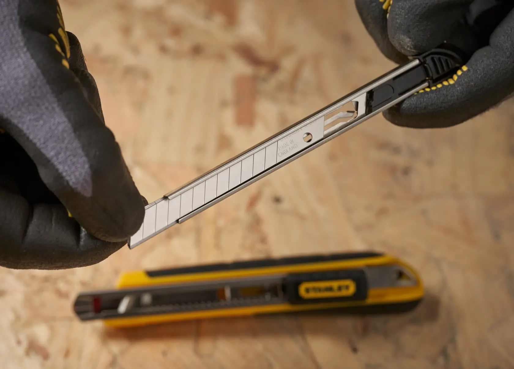 Photo of STANLEY 0-11-300 snap-off utility knife blade being replaced, with gloved hands, on wood surface.