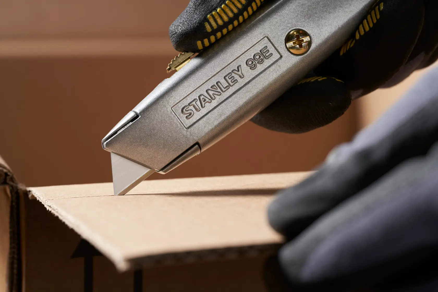 STANLEY 0-11-911 utility knife cutting cardboard, close-up side view, worker wearing black gloves.
