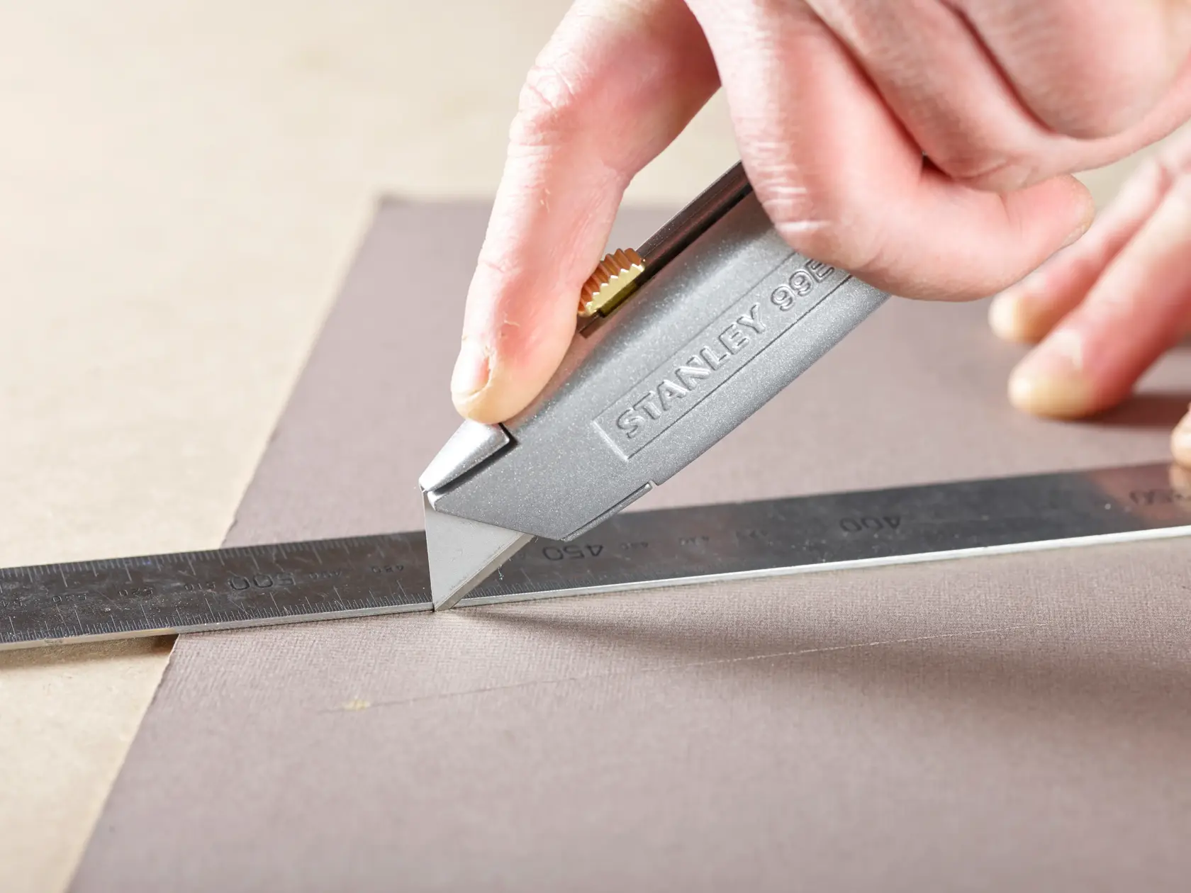STANLEY 0-11-911 utility knife cutting along metal ruler on fabric, close-up photography.