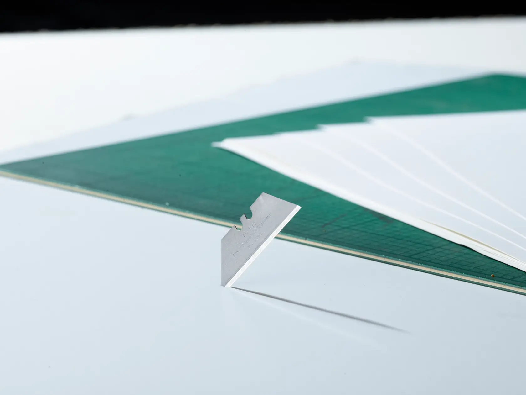 STANLEY 0-11-911 photography of single steel utility blade standing upright on white surface near green cutting mat.