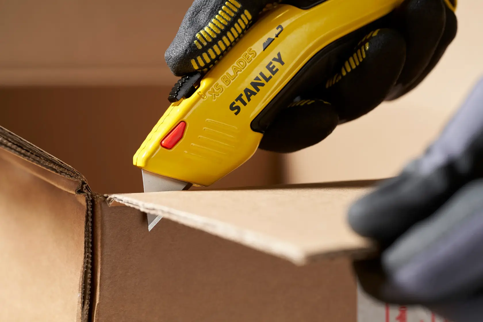 STANLEY 0-11-921 utility knife cutting cardboard, close-up, yellow handle, gloved hand.