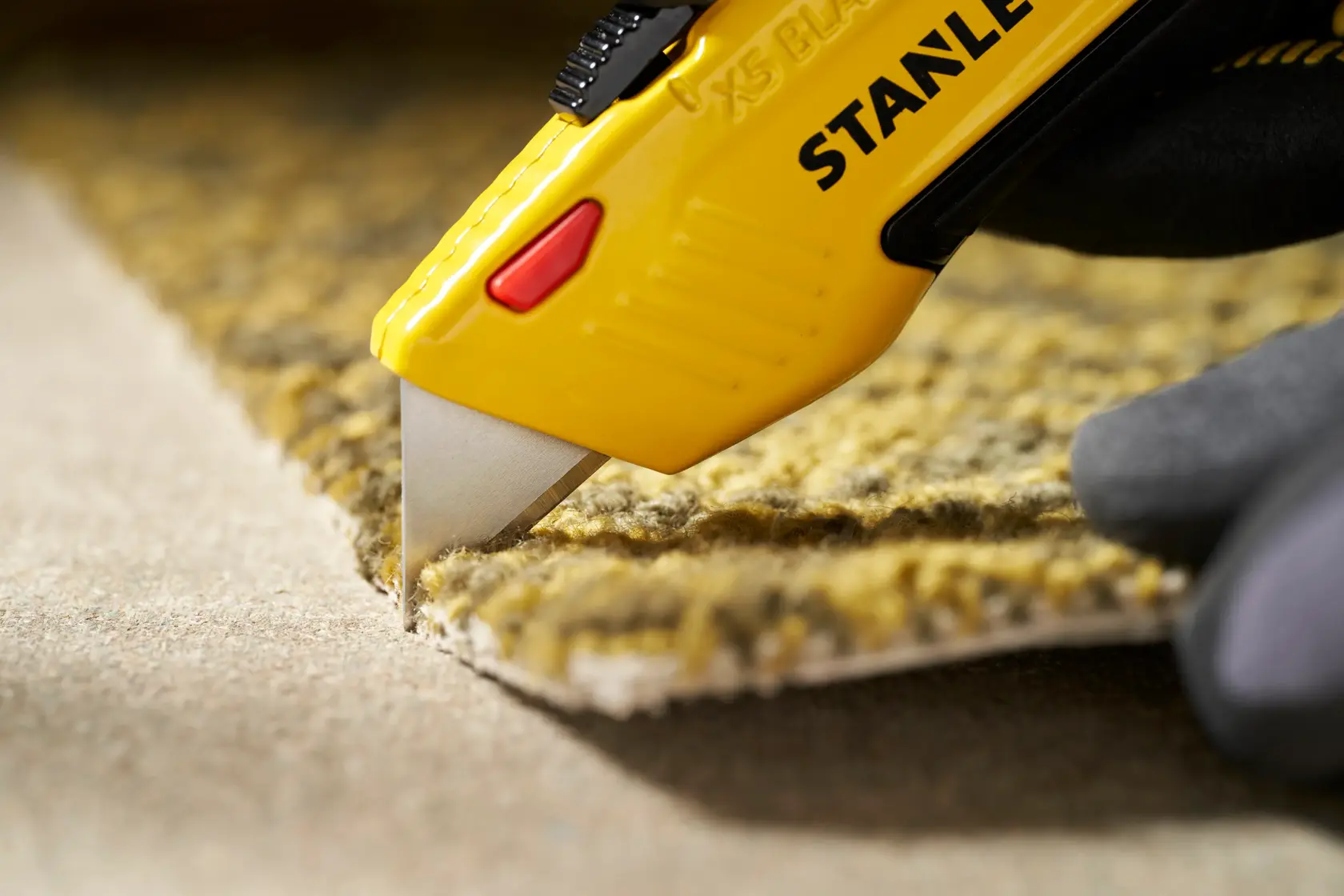 STANLEY 0-11-921 utility knife cutting yellow carpet, close-up photography of blade and handle.