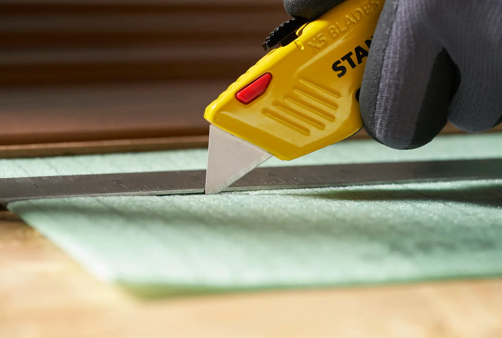 STANLEY 0-11-921 utility knife with yellow handle cutting material along a metal ruler, close-up view.