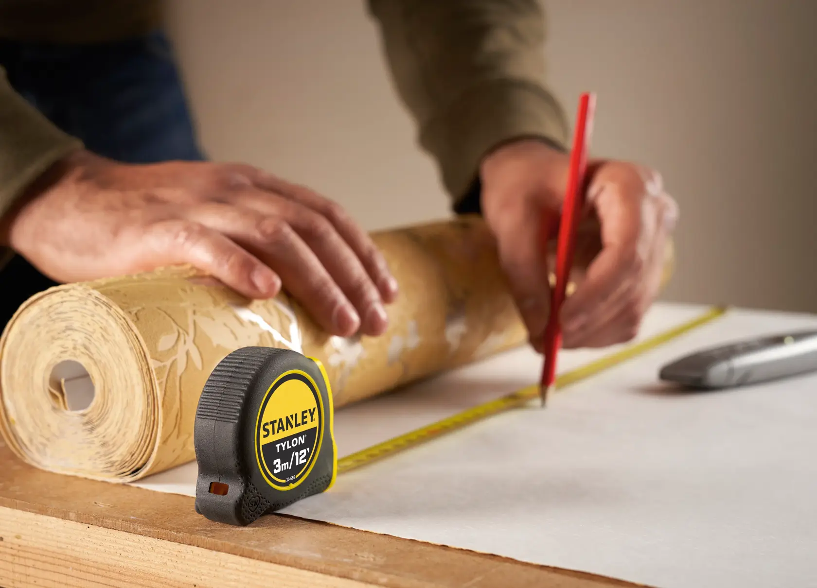 Photo of STANLEY 0-30-686 tape measure on a table with a wallpaper roll and hands measuring.