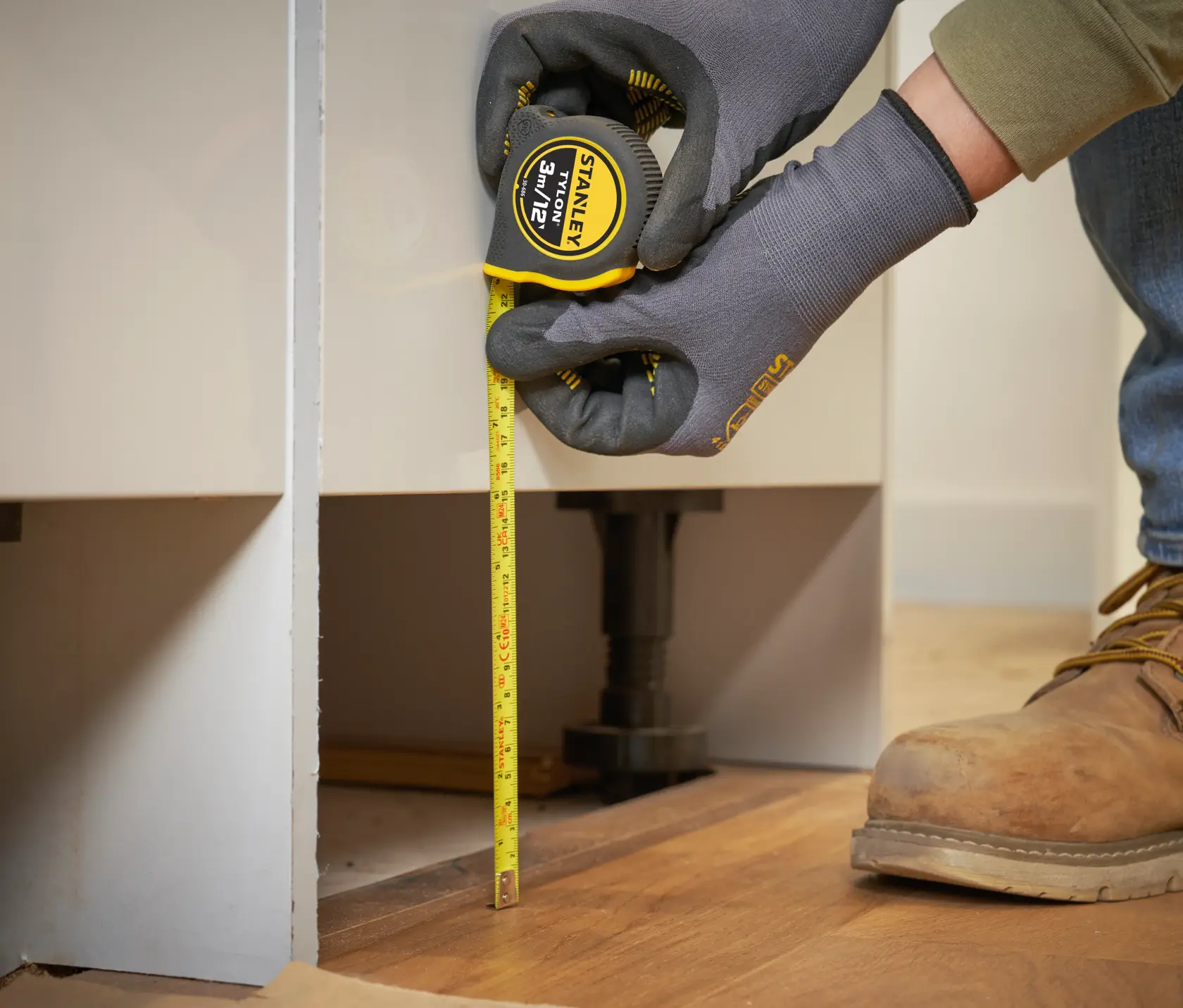 STANLEY 0-30-686 tape measure, yellow, used for vertical measurement against cabinet on wooden floor.