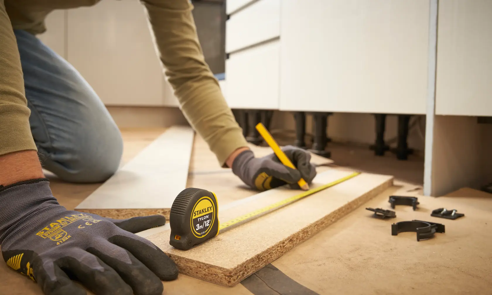 STANLEY 0-30-686 tape measure on wood plank, person measuring and marking with pencil, close-up workshop scene.