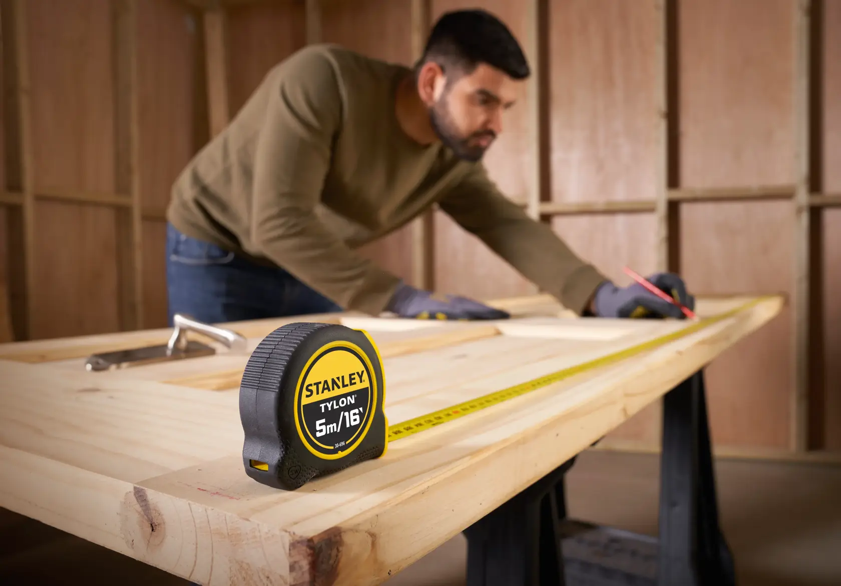 STANLEY 0-30-696 tape measure on a wooden workbench, close-up angle, with worker marking wood.