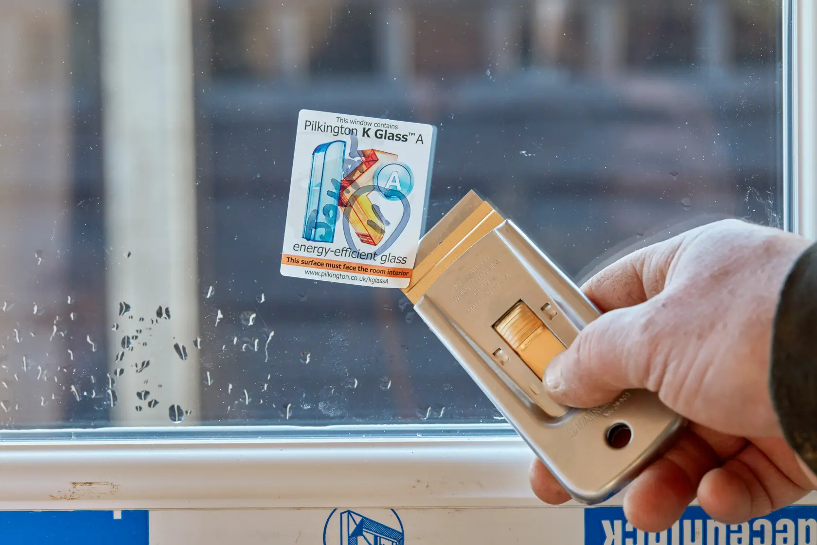 STANLEY 1-11-515 utility blade scraper in hand removing sticker from glass window, close-up angle.