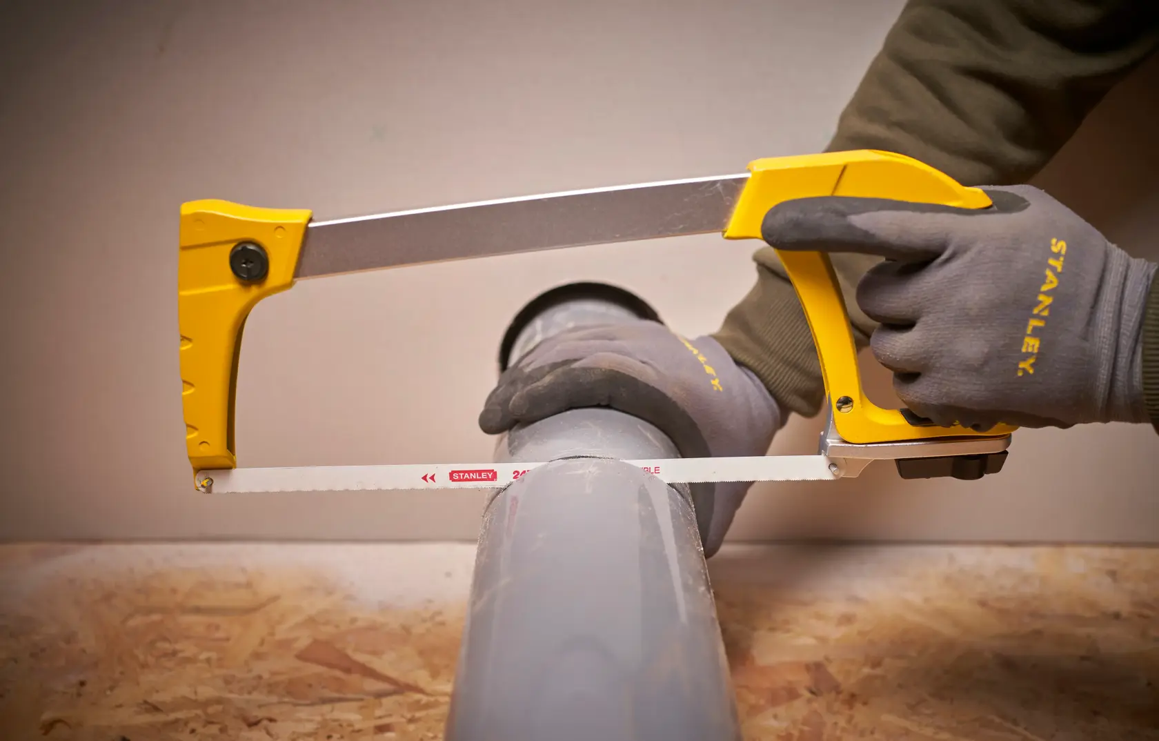 STANLEY 1-20-110 hacksaw cutting grey pipe, close-up view, with worker wearing STANLEY gloves.