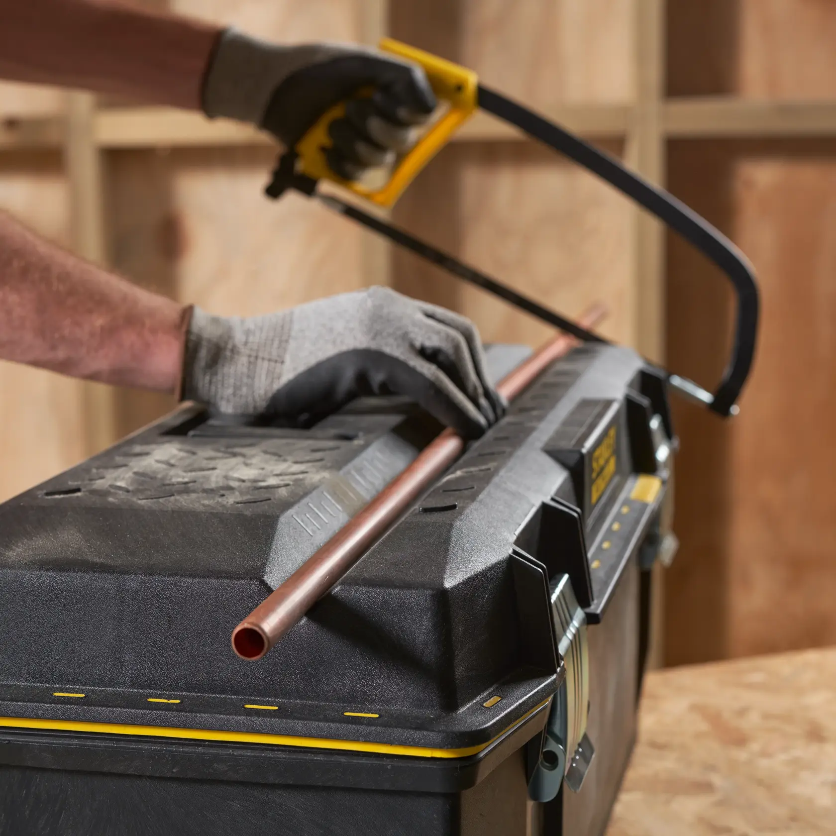 STANLEY 1-93-935 toolbox used as work surface, gloved hands cutting copper pipe with hacksaw, front angle