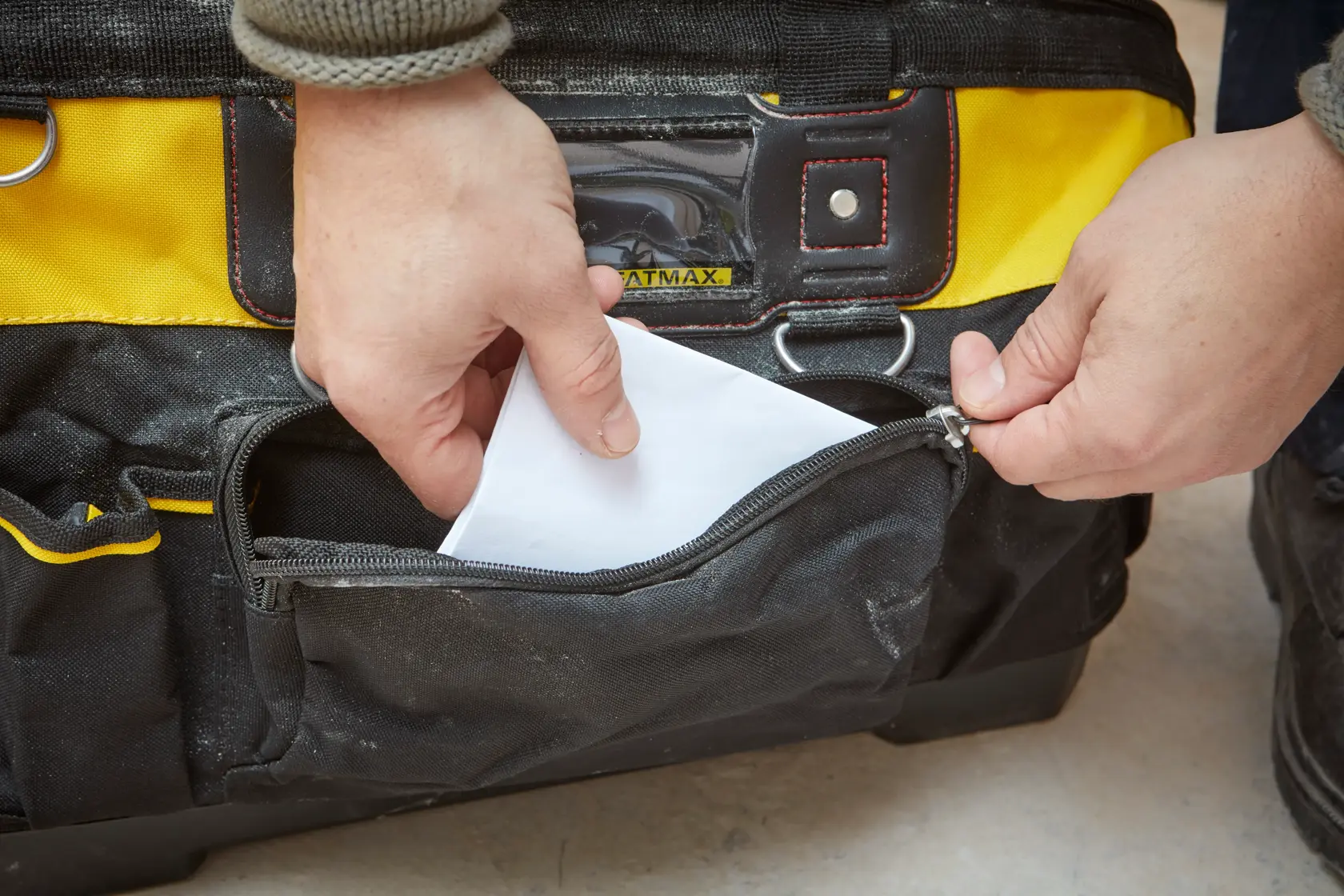 STANLEY 1-93-950 tool bag front pocket with zipper being opened and paper being placed inside.