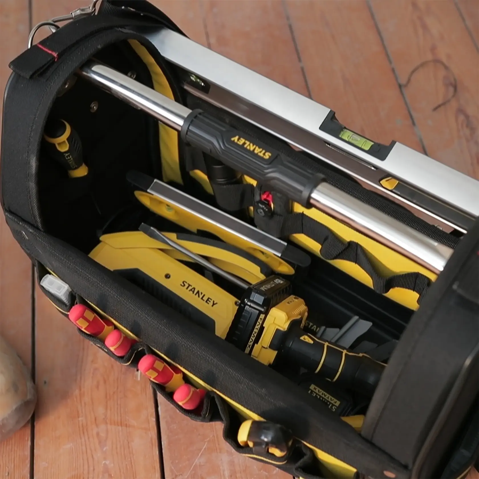 STANLEY 1-93-951 tool bag top view with yellow and black hand tools and level on wood floor.