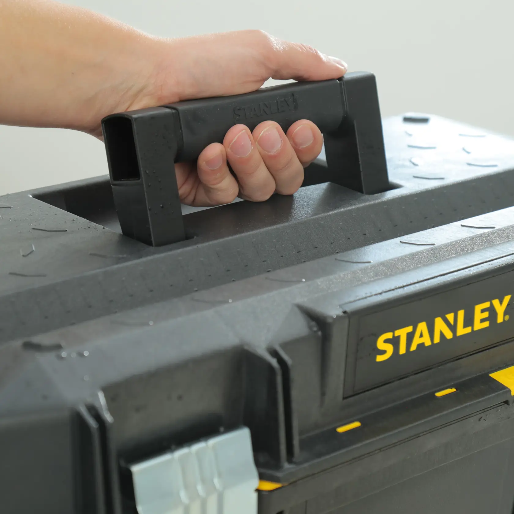 STANLEY 1-94-749 black toolbox handle close-up, hand holding, yellow logo visible.