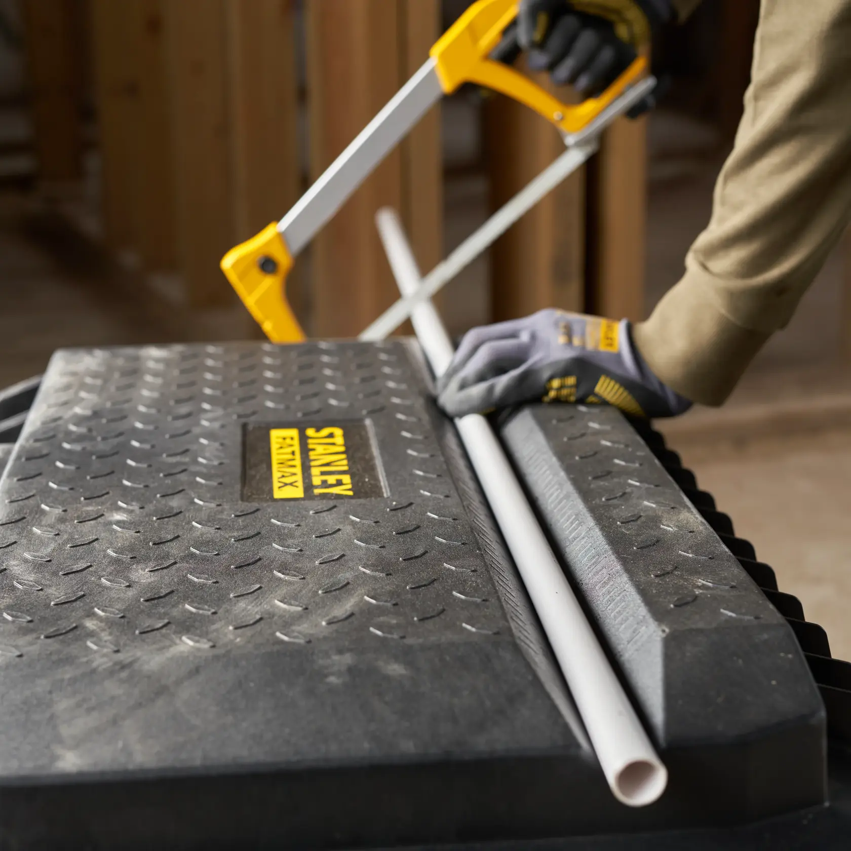Stanley 1-94-850 toolbox used as work surface, gloved hand sawing PVC pipe with Stanley saw.