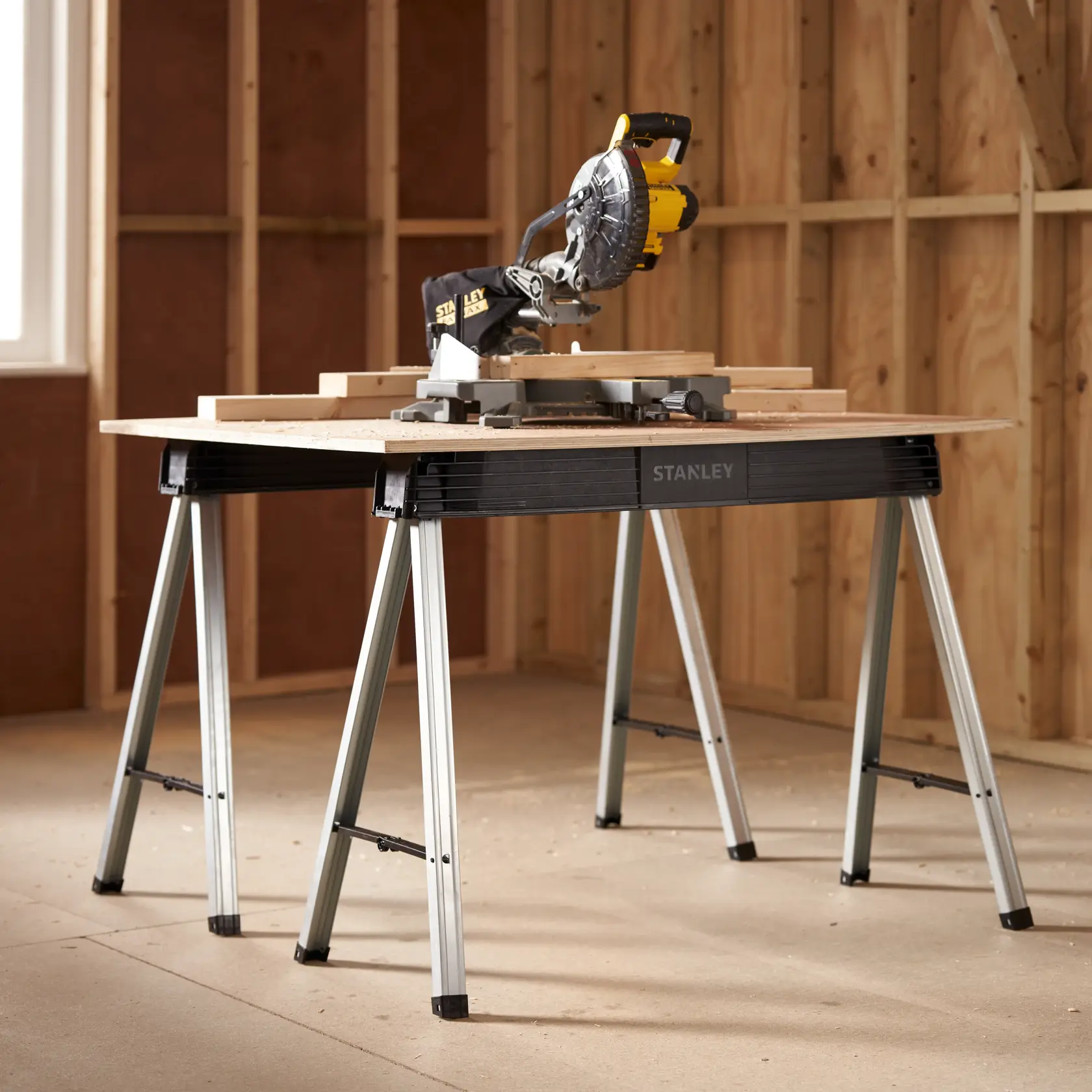 STANLEY 1-97-475 folding workbench with metal legs, shown in a workshop with a miter saw on top.