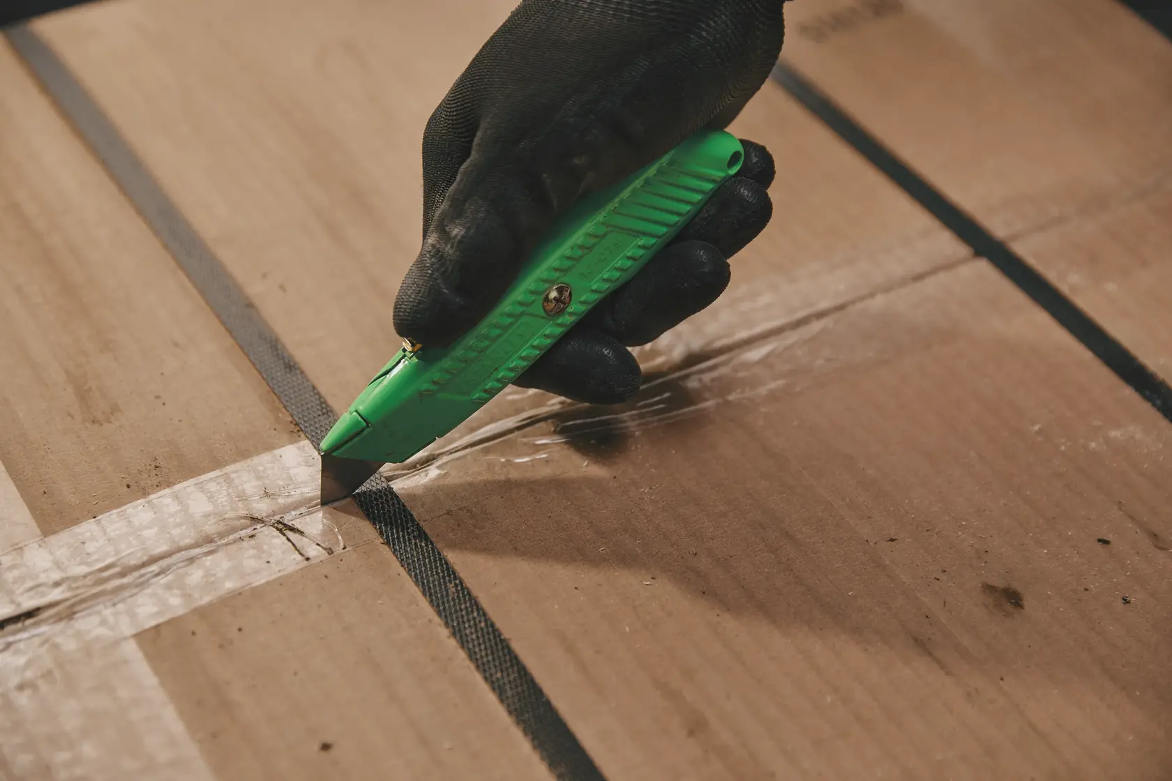 Photo of STANLEY 10-179 utility knife cutting tape on a cardboard box, gloved hand holding green knife.