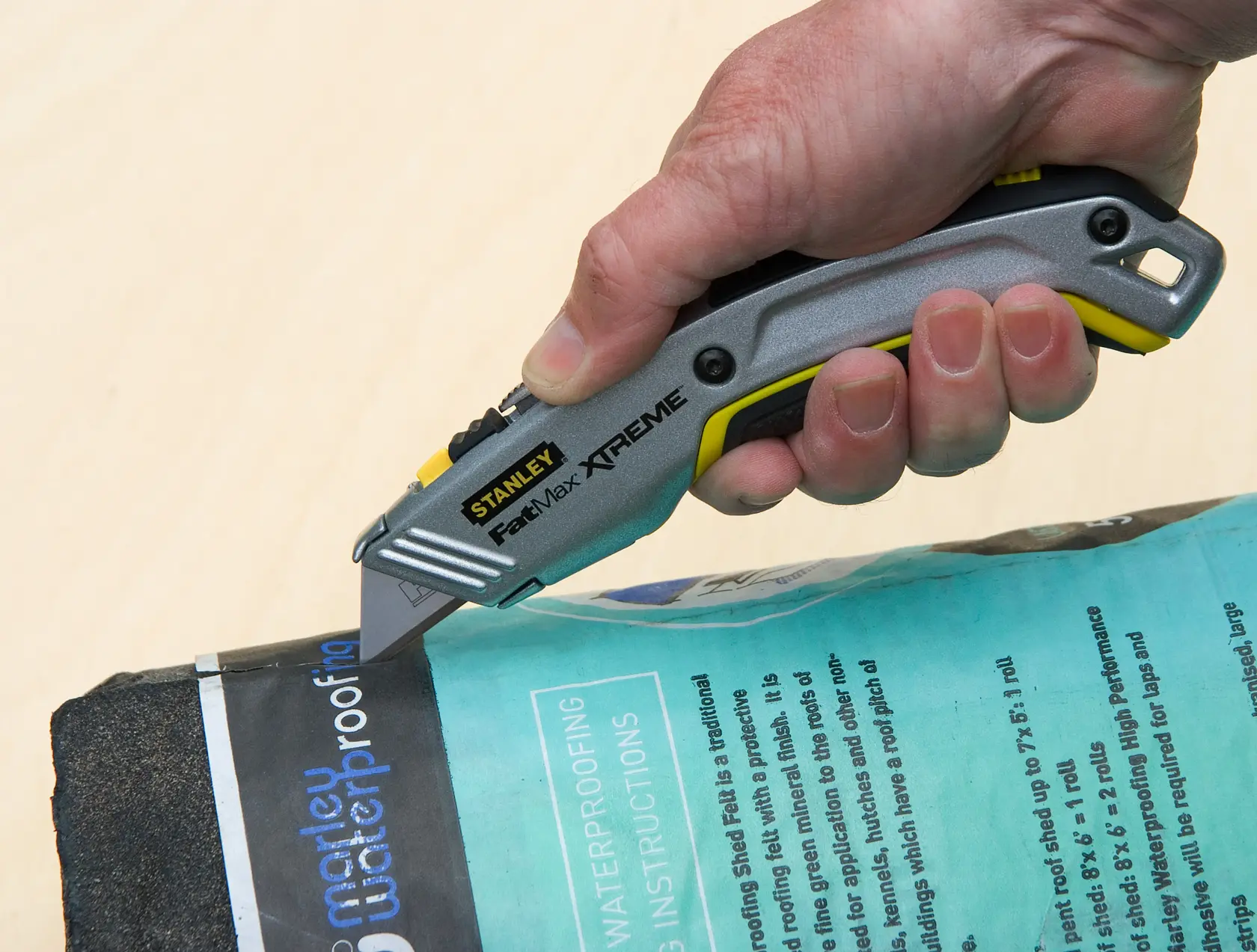 Photo of STANLEY 10-789 utility knife cutting waterproofing material, close-up view of tool in hand.