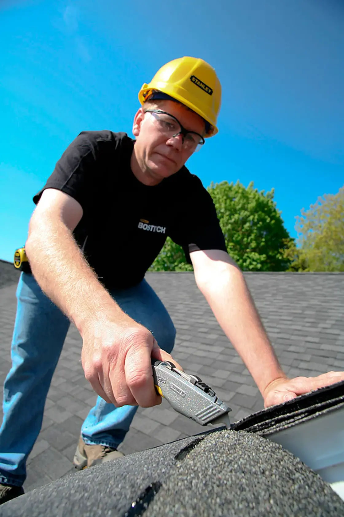Photo of a worker using STANLEY 10-789 utility knife to cut roof shingles outdoors.