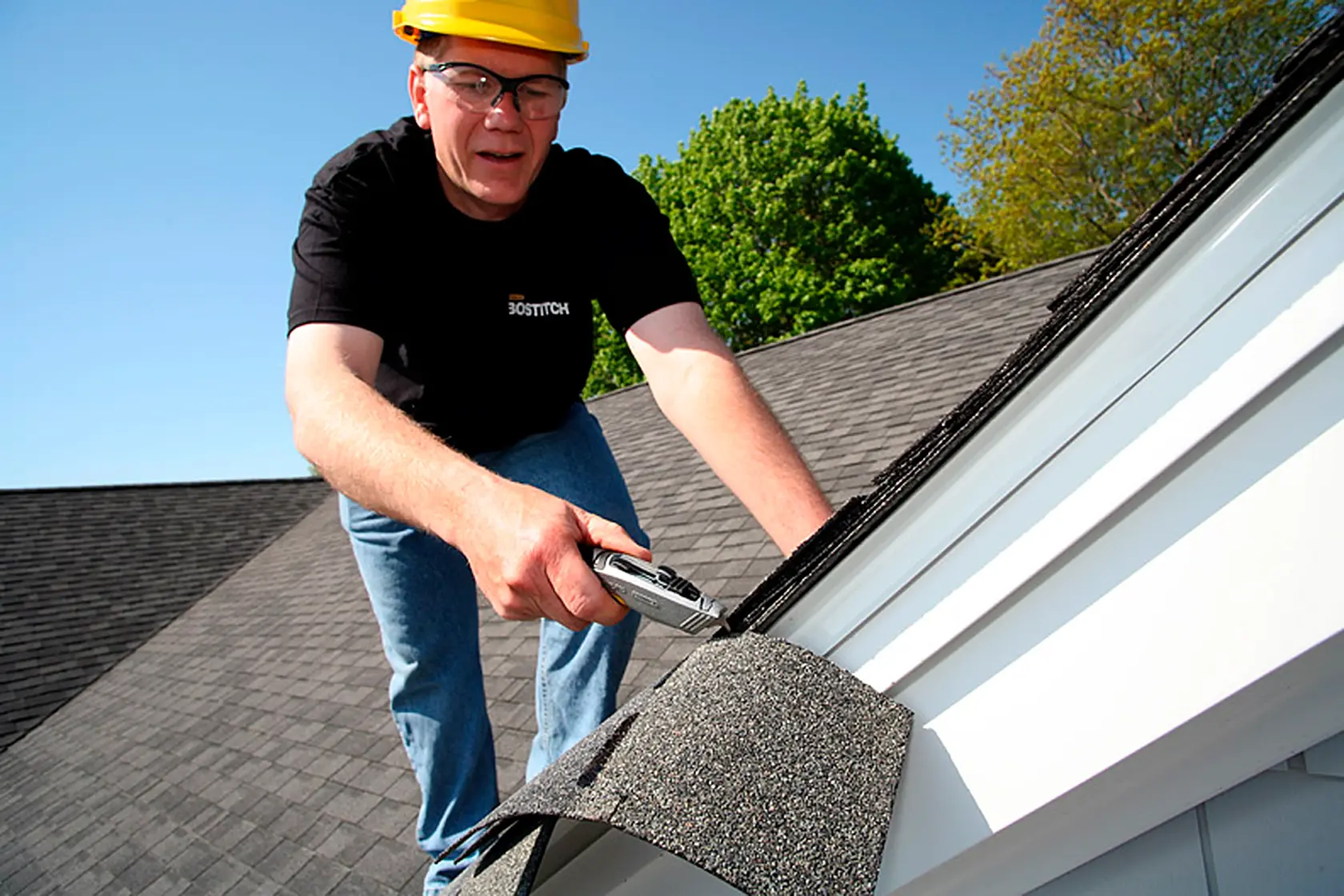 STANLEY 10-789 utility knife in use cutting roofing shingles on a house roof, outdoor setting.