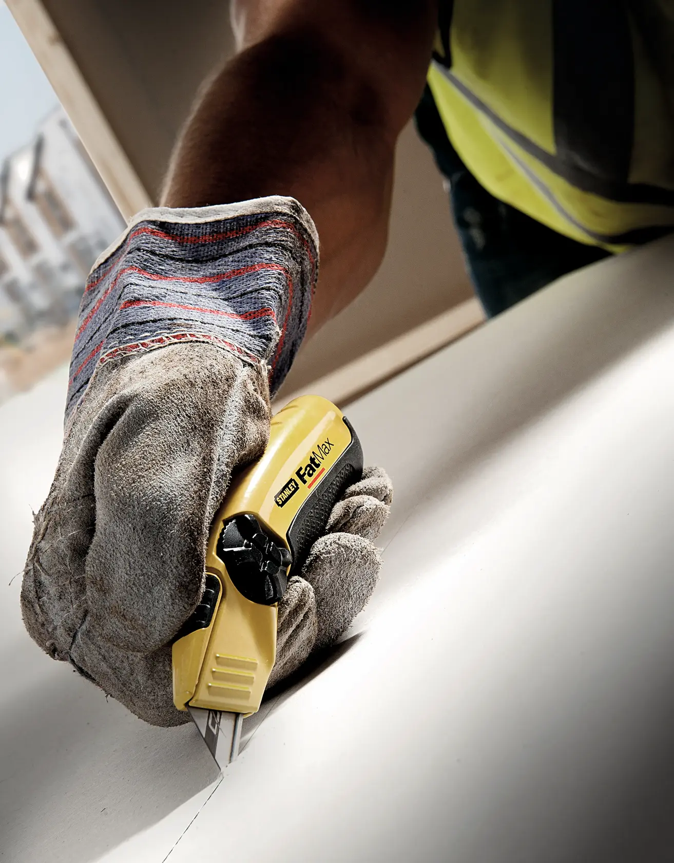STANLEY 11-800 FatMax utility knife cutting drywall with gloved hand, close-up photography.