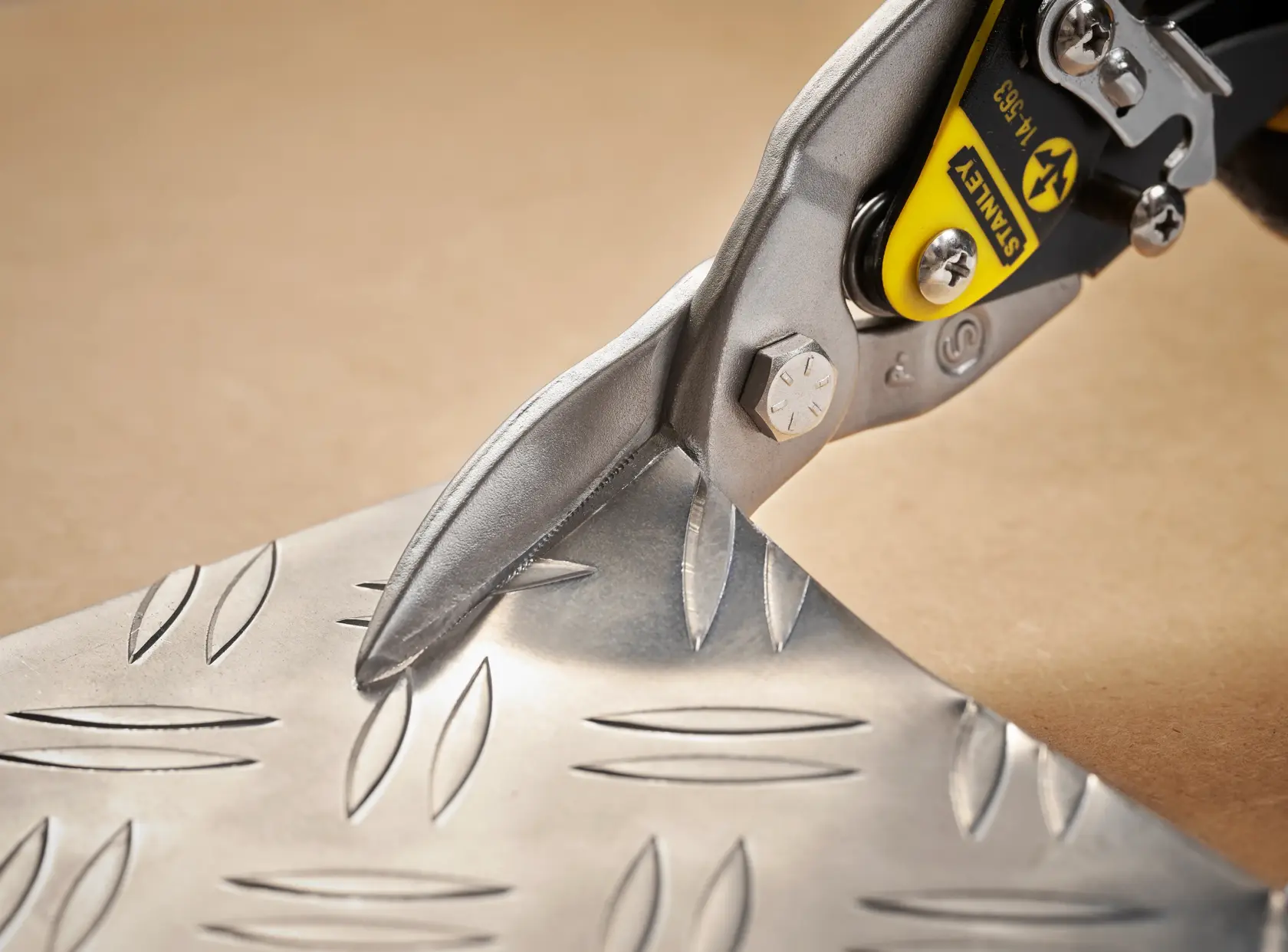 STANLEY 14-564 aviation snips cutting patterned metal sheet, close-up angle, tool photography.