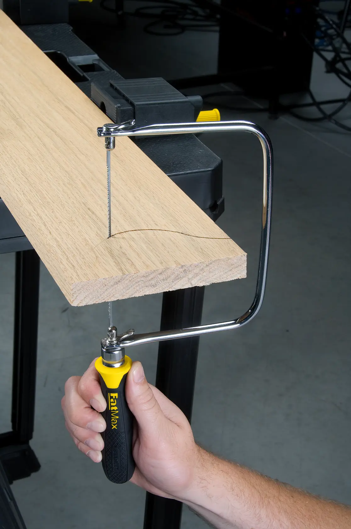 STANLEY 15-104 coping saw with yellow and black handle cutting curved line in wood, close-up side view.