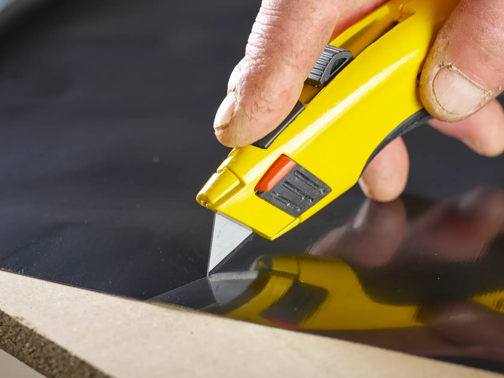 STANLEY 2-11-921 utility knife with yellow handle cutting black sheet, close-up, product in use.