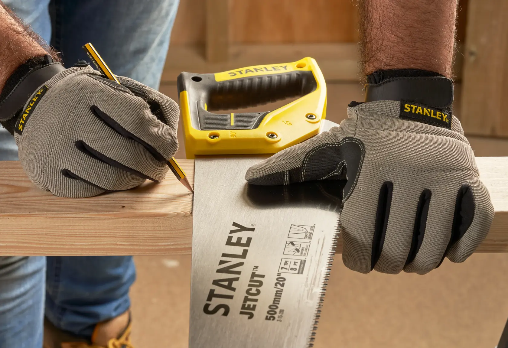 STANLEY 2-15-288 hand saw and yellow stapler on wood, person with gloves marking cut line, workshop background.