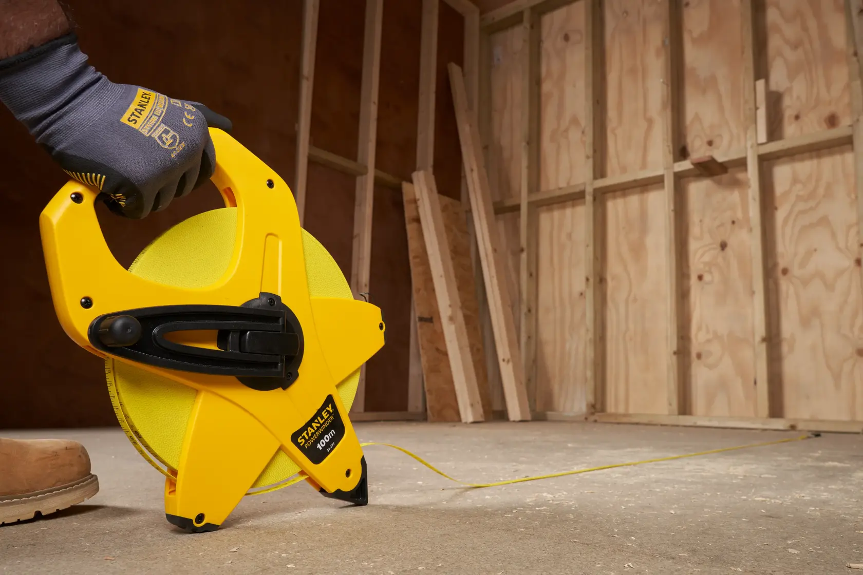 STANLEY 2-34-777 open reel tape measure, yellow casing, used for measuring on construction floor.