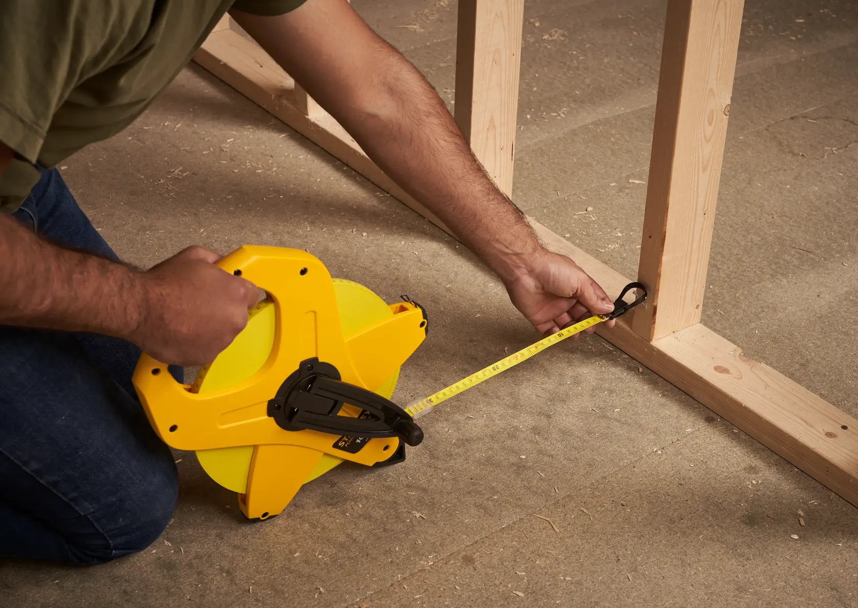 STANLEY 2-34-777 tape measure in use measuring wood framing, side angle, yellow casing.