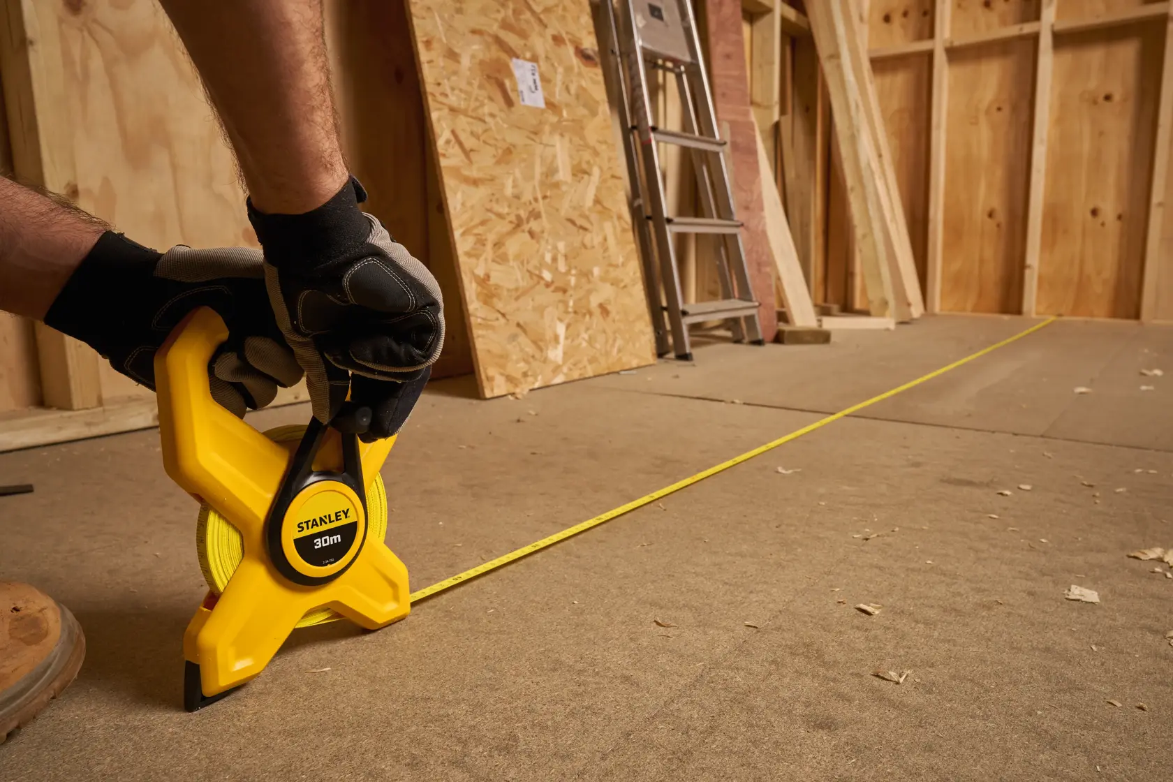 Photo of STANLEY 2-34-792 tape measure with 30m yellow blade in use on construction floor, gloved hand holding tool.