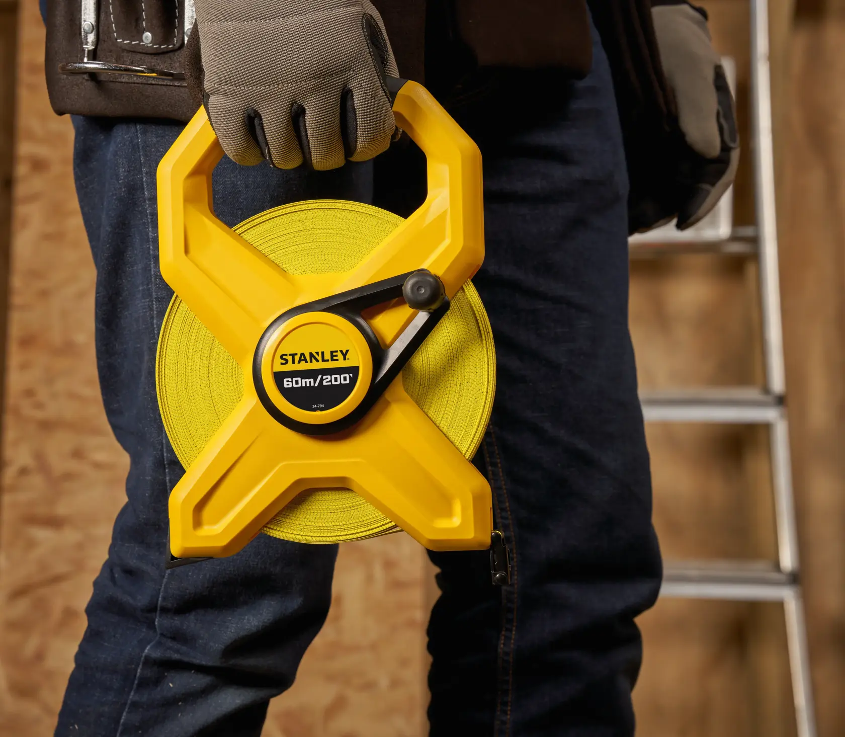 Photo of STANLEY 2-34-794 yellow open reel tape measure held by a person wearing gloves, construction background.