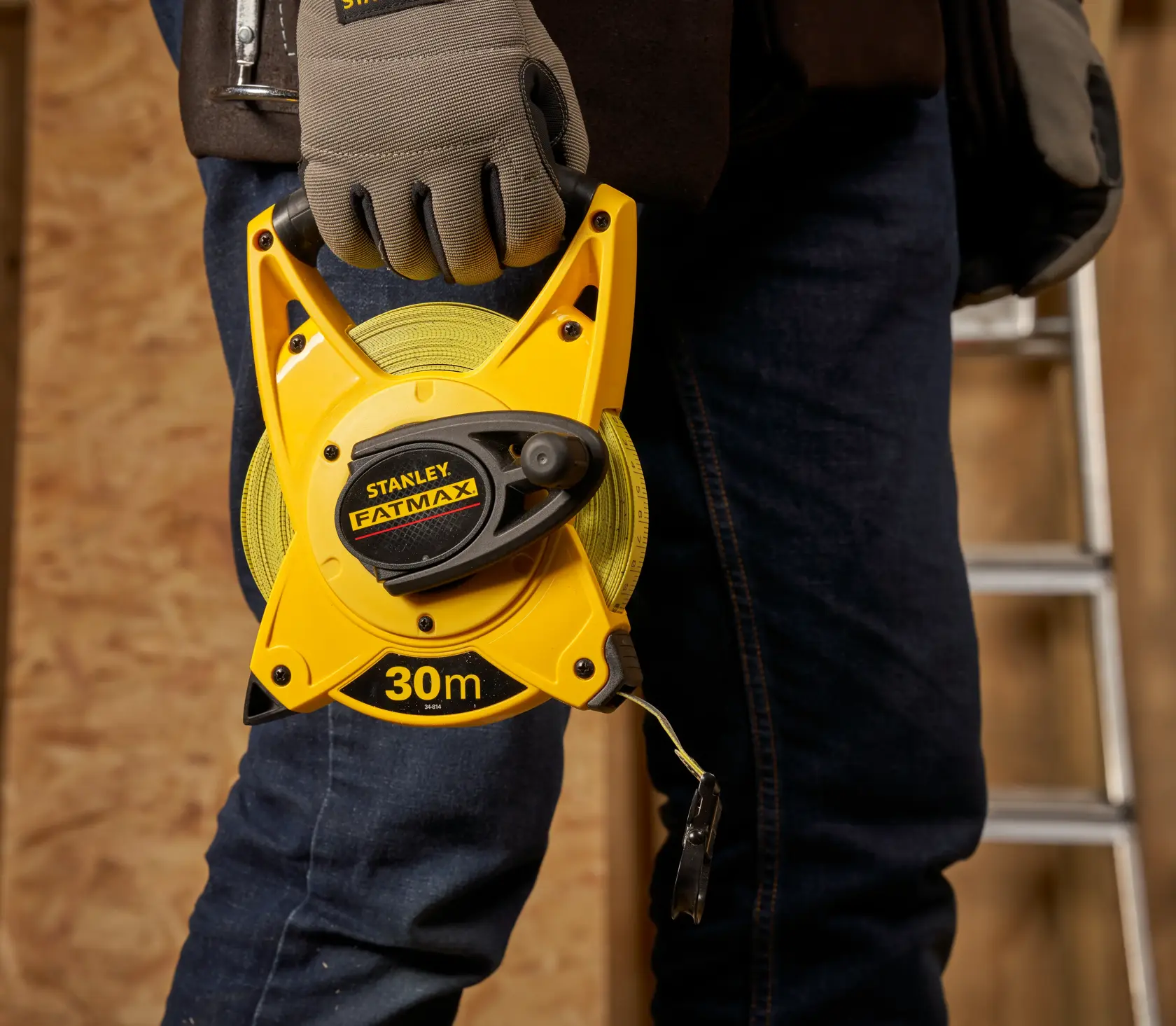 STANLEY 2-34-814 open reel 30m FATMAX tape measure held by a gloved hand, workshop background.