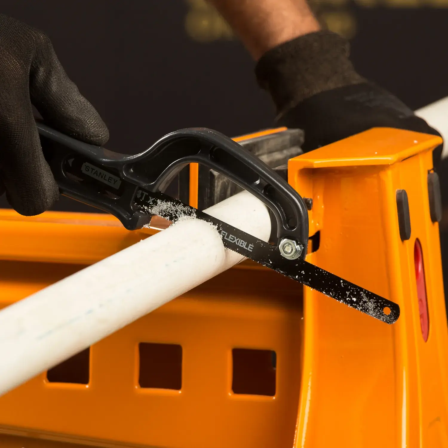 STANLEY 20-807 mini hacksaw cutting white PVC pipe on orange workbench, close-up side angle.