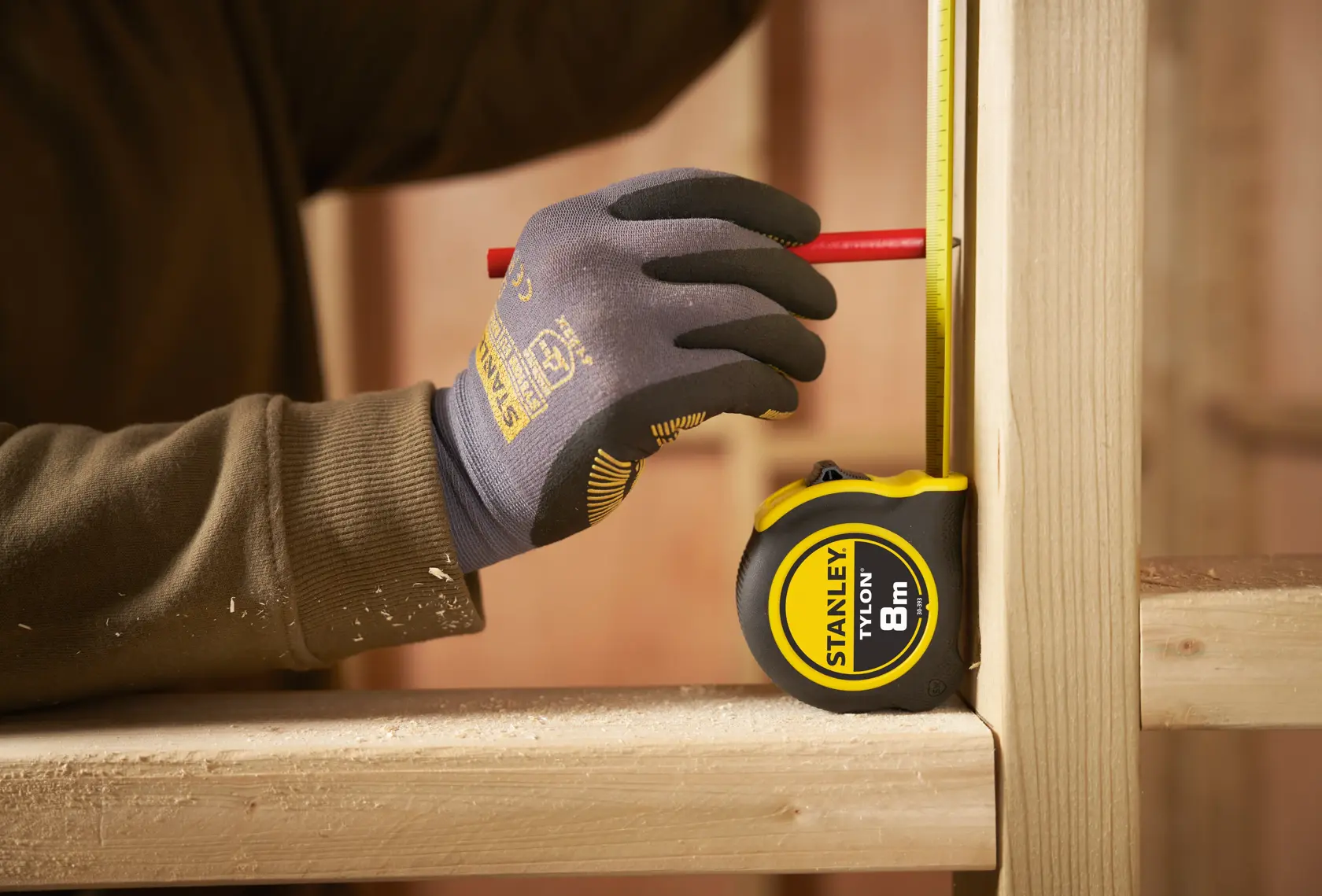 Photo of STANLEY 30-393 tape measure on wood, gloved hand marking measurement with red pencil.
